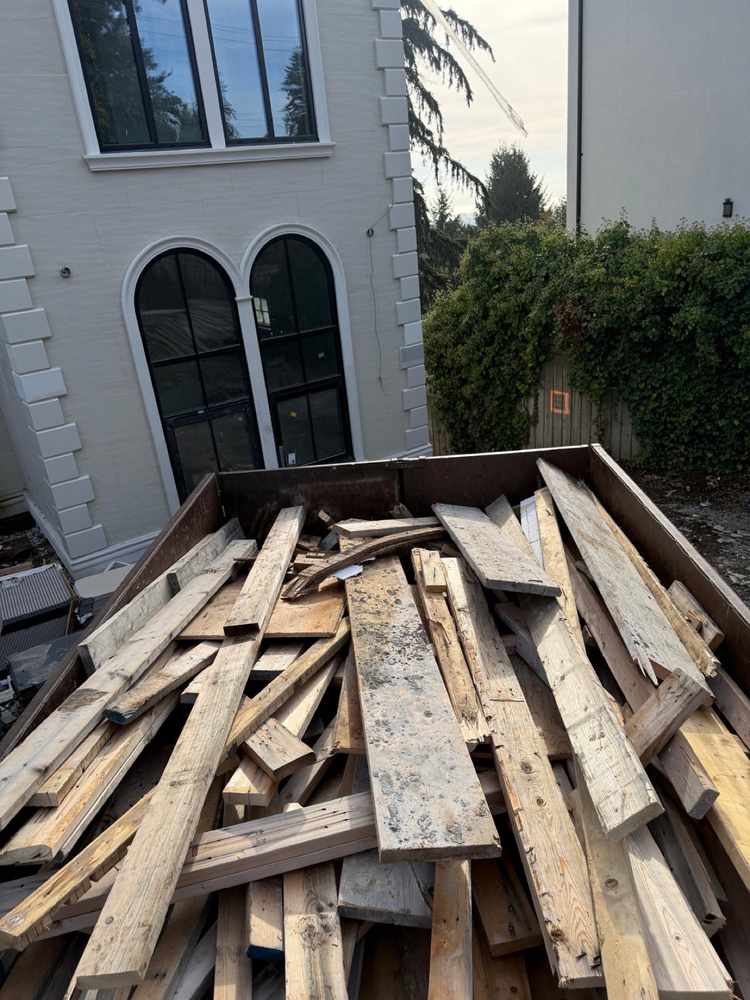 Dump trailer full of lumber and wood debris beside a house